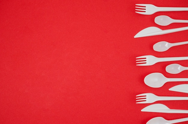 Plastic spoon and fork arranged in row on bright red backdrop