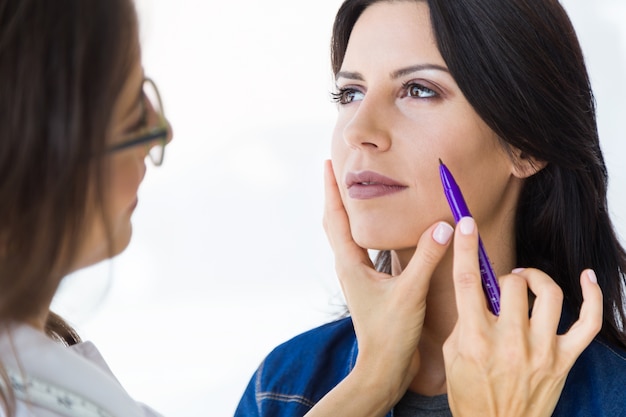 Plastic surgeon drawing dashed lines on her patient's face.