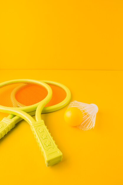 Пластиковая теннисная ракетка с мячом и воланом на желтом фоне