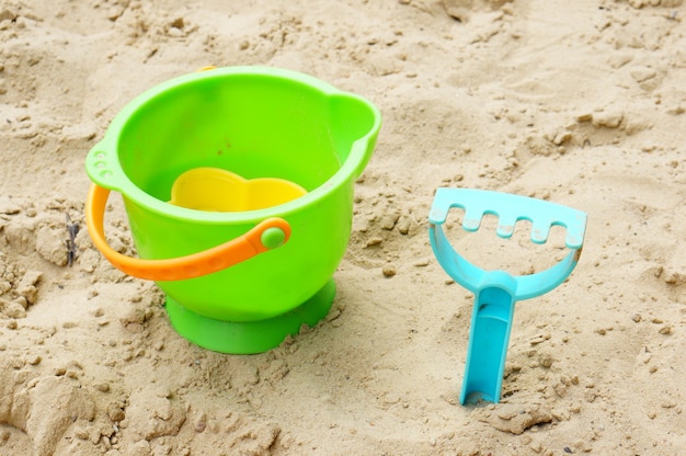 プラスチックのおもちゃのバケツと砂の上の青い砂の熊手