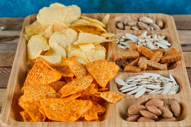 Plate of assorted snacks on a wooden table. Chips, crackers, almonds, pistachios, sunflower seeds.