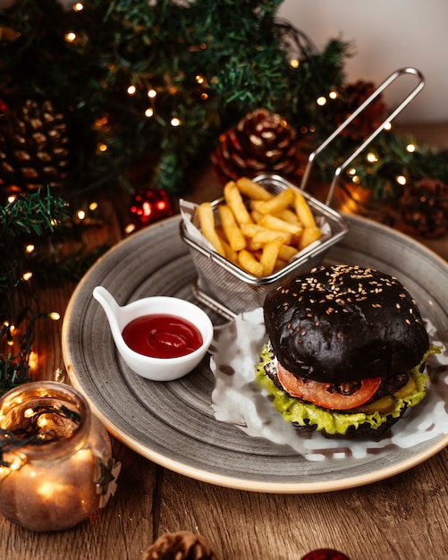 A plate of black beef burger served with french fries and ketchup