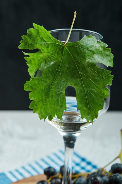 Free photo a plate of black grapes and a glass of wine with leaf on white table, close up