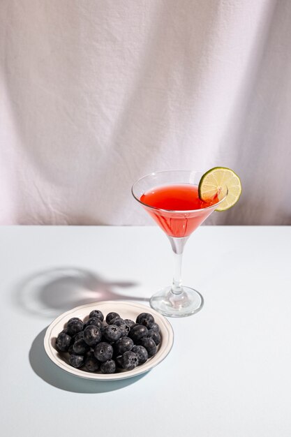Plate of blue berries with cocktail beverage above white desk