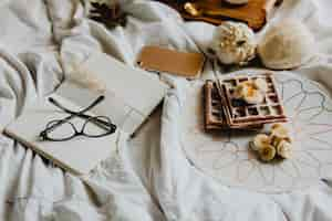 Free photo plate of breakfast waffle with banana topping on a white bed next to a diary and a phone