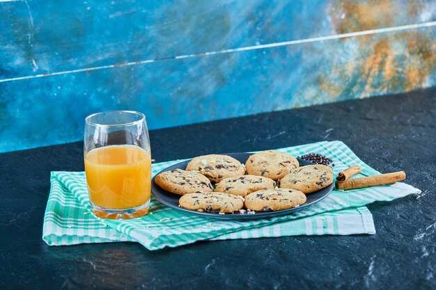 A plate of chocolate chips cookies and a glass of orange juice on dark table with cinnamon