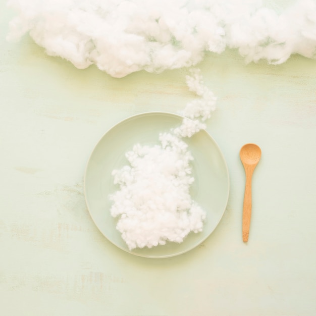 Plate of clouds and wooden spoon on color background