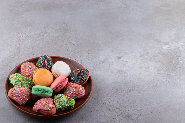 Plate of colorful cookies and macaroons with sprinkles on table.