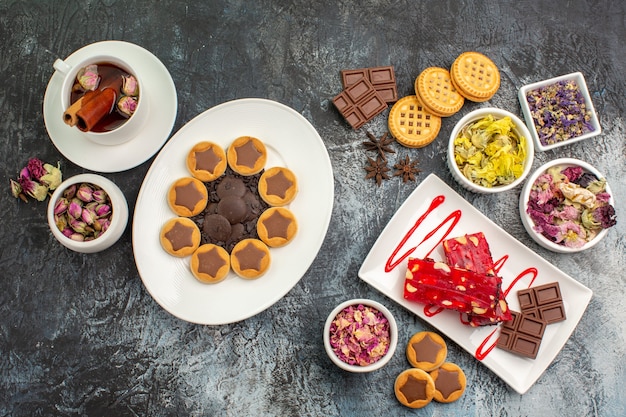 A plate of cookie and chocolate with a cup of herbal tea and dry flowers on grey