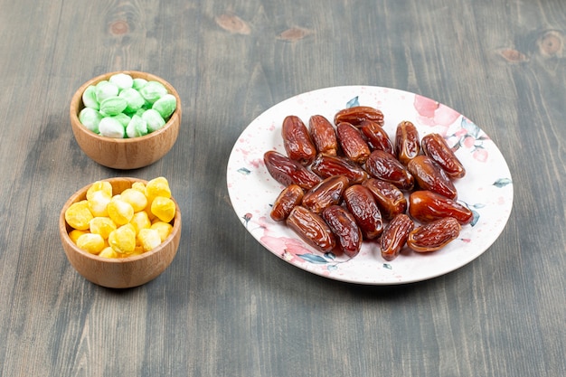 Plate of dates and colorful candies on wooden surface
