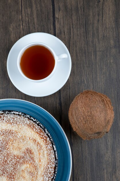 A plate of delicious pie with fresh whole coconut placed on a wooden table .