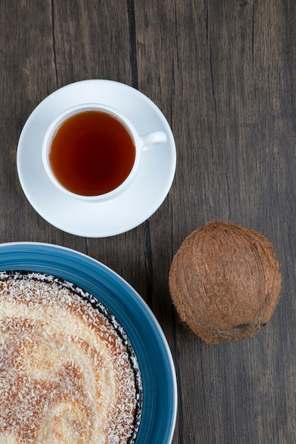 Тарелка вкусного пирога со свежим цельным кокосом на деревянном столе.