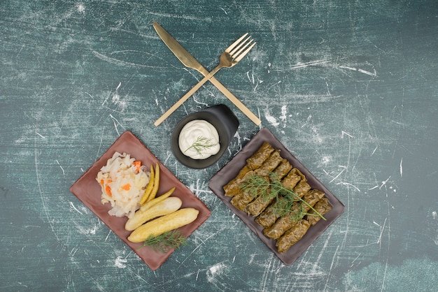 Plate of dolma and sour cream with salt cucumber and cabbage on marble surface