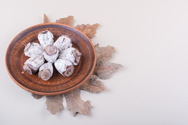 Plate of dried persimmons and dry leaves on white background. High quality photo