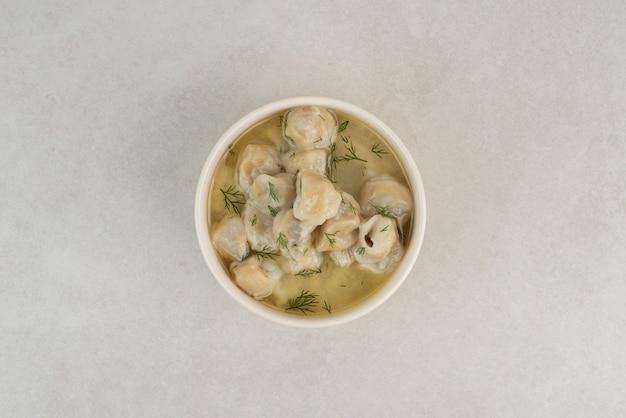 Plate of dumplings with greens on white table.