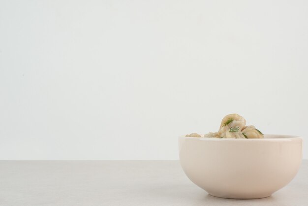 Plate of dumplings with greens on white table.