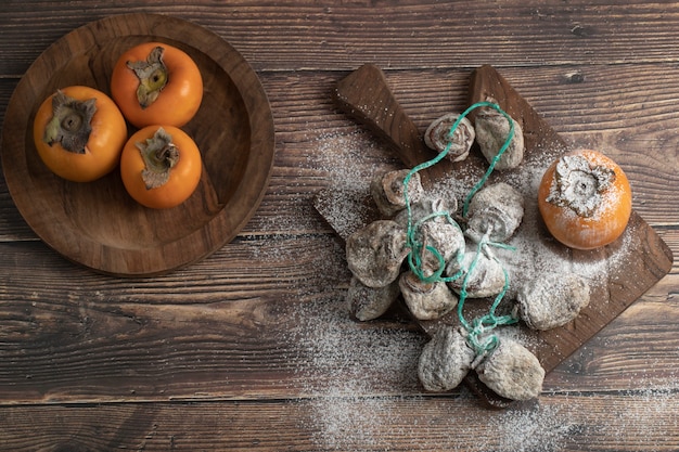 Plate of fresh fuyu and dried persimmon fruits on wooden board