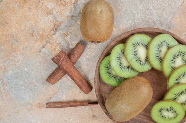 Plate of fresh kiwi and cinnamon sticks on marble surface. high quality photo