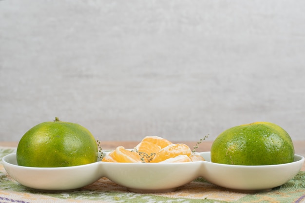 Plate of fresh mandarines on marble table with tablecloth.