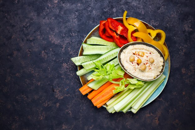 Тарелка салата из свежих органических овощей с хумусом на темно-коричневой или бетонной поверхности