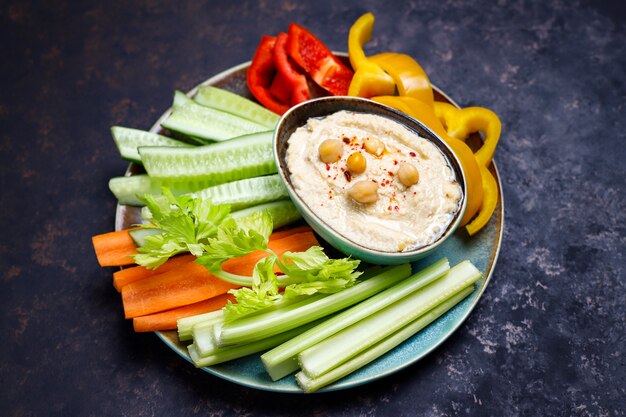 Plate of fresh organic vegetables salad with hummus on dark brown or concrete surface 