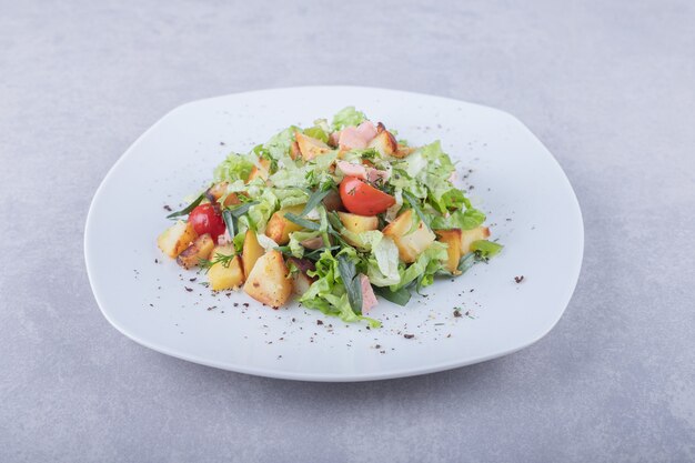 Plate of fresh salad with sausages on stone background.