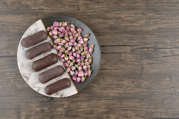 A plate full of chocolate cream rolls with cream of milk with dried roses on a wooden table.