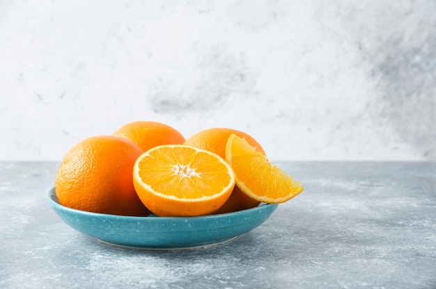 A plate full of sliced and whole juicy orange fruits on stone table .