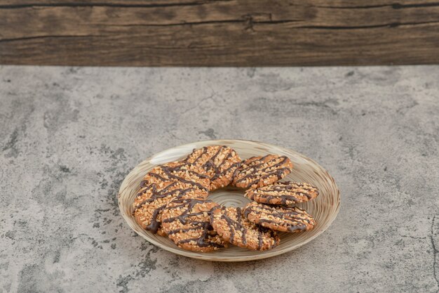 Plate full of sweet oatmeal cookies with chocolate syrup on a stone background .