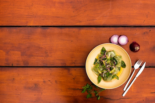 Plate of garnish green ravioli pasta with onion on wooden table