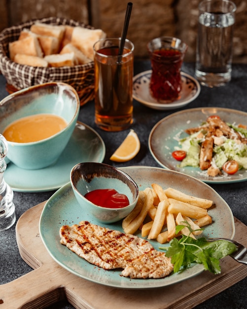 A plate of grilled chicken breast served with french fries and ketchup