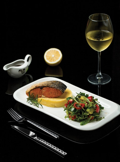 Foto gratuita un piatto di filetto di salmone alla griglia con spezie e insalata verde servito con un bicchiere di vino italiano