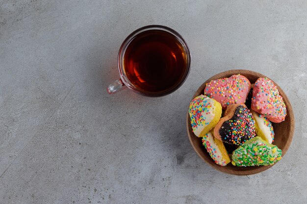 A plate of heart shaped cookies with sprinkles and a cup of hot tea . 