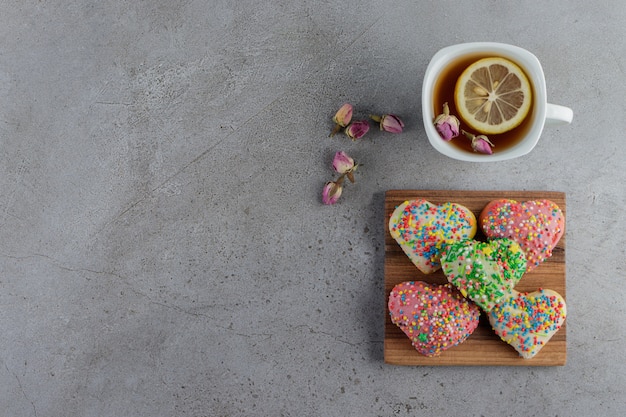 A plate of heart shaped cookies with sprinkles and a cup of hot tea 