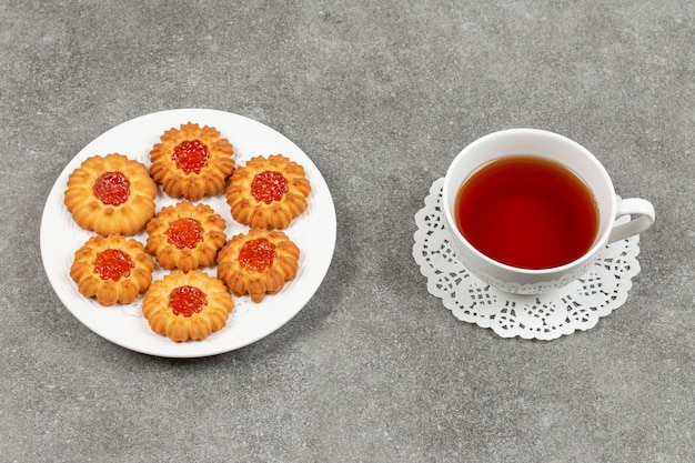 Plate of jelly biscuits and cup of tea on marble surface