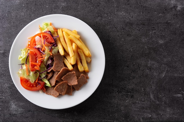 Plate of kebab, vegetables and french fries on black stone background