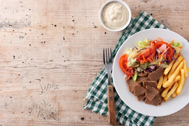 Plate of kebab, vegetables and french fries on wooden table