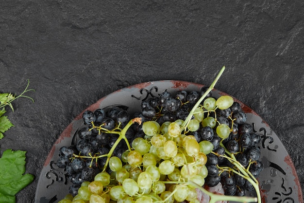 A plate of mixed grapes with leaves on dark background. High quality photo