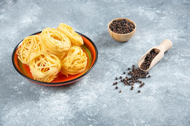 Plate of noodles and pepper grains on marble background.