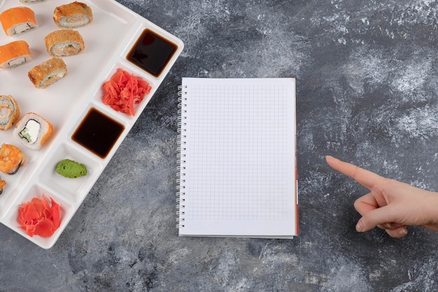 Тарелка вкусных суши-роллов и пустой блокнот на мраморном фоне