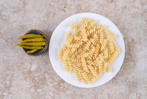 Plate of pasta and a small bowl of pickled peppers on marble surface