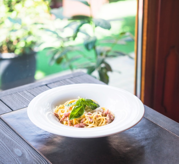 Plate of pasta spaghetti with basil leaves on placemat over the table