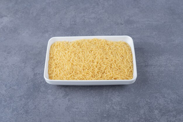 Plate of raw macaroni on stone background.