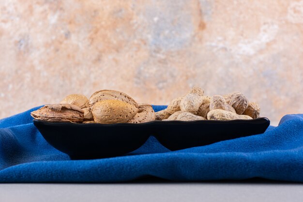 Plate of raw shelled almonds and peanuts on blue cloth. High quality photo