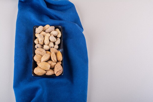 Plate of raw shelled almonds and peanuts on blue cloth. High quality photo