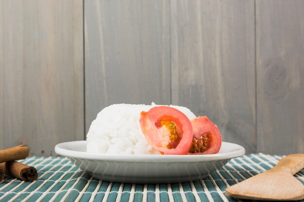 Plate of rice with tomato slice; cinnamon sticks and wooden spatula on placemat