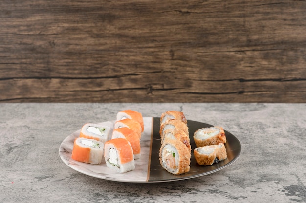 Plate of salmon and hot sushi rolls placed on marble table