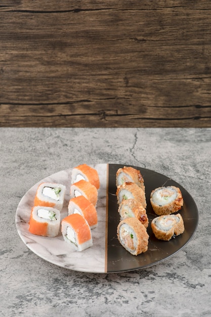 Plate of salmon and hot sushi rolls placed on marble table
