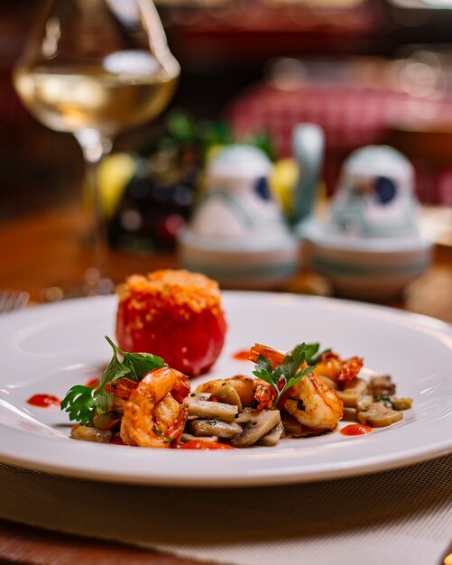 A plate of sauteed mushroom and shrimp served with tomato