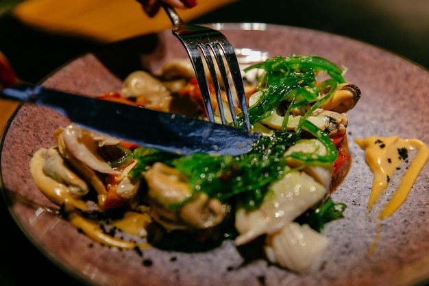 Тарелка с салатом из морепродуктов с соусом. Вилка и нож. Концепция питания.